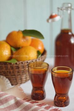 two shot glasses filled with liquid next to a basket of oranges on a table