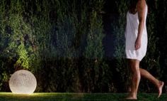 a woman in white dress walking next to a large light ball on grass covered ground