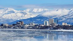 a city with mountains in the background and ice on the water below it, as seen from across the river