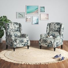 two chairs sitting on top of a rug in front of a wall with pictures above them