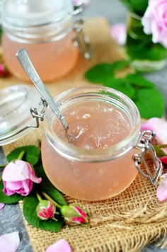 two jars filled with pink flowers on top of a table next to some spoons