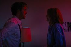 a man and woman standing next to each other in a room with red light coming from the ceiling