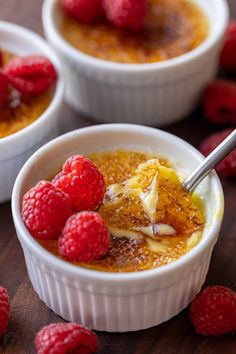 three small bowls filled with pudding and raspberries on top of a wooden table