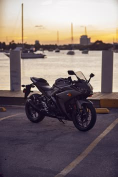 a motorcycle is parked in the parking lot next to some water and boats at sunset