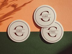 three circular business cards with the word cleo on them sitting next to a plant