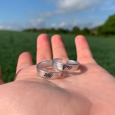 two silver rings with initials on them are held in someone's hand