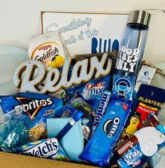 a box filled with candy and snacks on top of a bed next to a sign