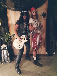 two men dressed up in costumes and holding guitars, standing next to each other on stage