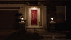 a red door is lit up at night in front of a house with two lights on