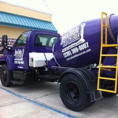 a large purple truck parked in front of a building with a yellow ladder on it's side