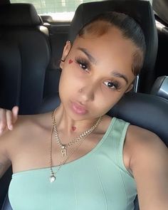 a woman sitting in the back seat of a car wearing a crop top and necklace