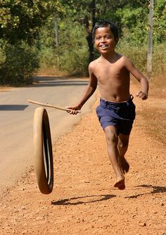 a young boy is running down the road with a stick in his hand and an advertisement for