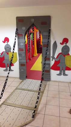 an indoor play area for children with castle doors and chains hanging from the ceiling, in front of a wall painted with cartoon characters