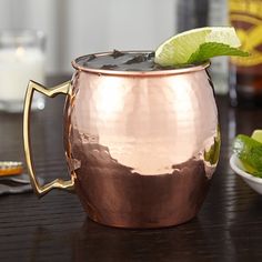 a close up of a metal cup on a table with limes and other drinks