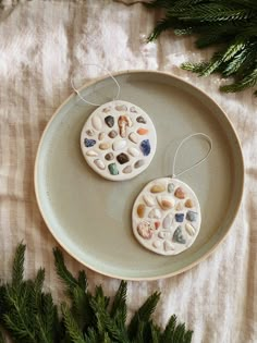 two ceramic ornaments are sitting on a plate next to some fir branches and pine needles