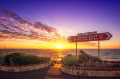 the sun is setting over the ocean and there are two signs pointing to different directions