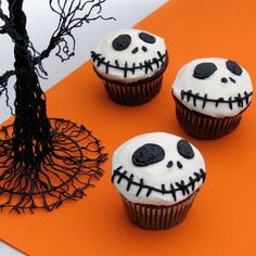 three cupcakes with white frosting and black icing decorated as jack - o'- lantern faces