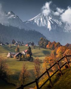 the mountains are covered in clouds and trees with houses on them, near a fence