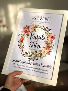 a person holding up a framed poster with the words kutub and shei written in arabic