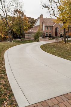 an empty driveway in front of a large house with lots of trees and leaves on the ground