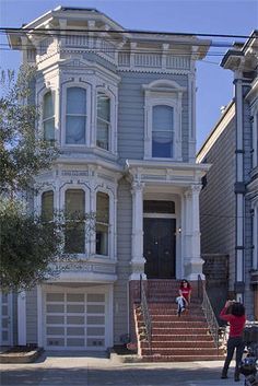 two people are standing in front of a house with stairs and garages on the street