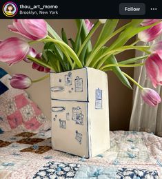 a vase filled with pink tulips on top of a bed next to a window