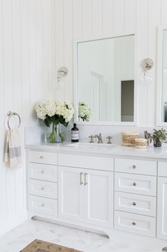 a bathroom with white cabinets and flowers in vases on the counter top, along with a rug