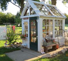 a small white greenhouse sitting on top of a lush green field next to a tree