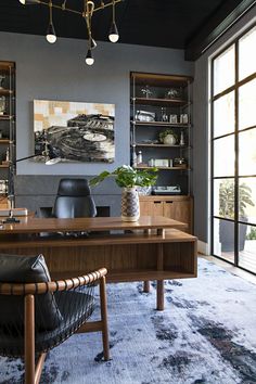 an office area with a desk, chair and bookcase on the wall next to large windows