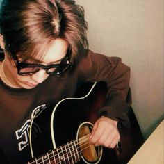 a young man with glasses playing an acoustic guitar