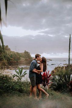 a man and woman embracing each other in front of the ocean on a cloudy day