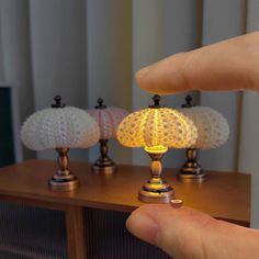 a hand is holding a small lamp in front of three other lamps on a table