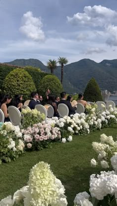 a group of people sitting in chairs on top of a lush green field next to flowers