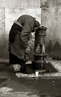 an old woman drinking water from a fire hydrant