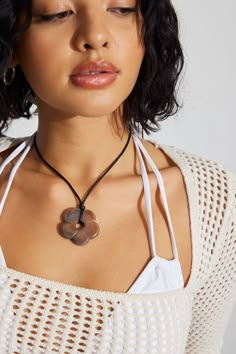 a woman with her eyes closed wearing a white sweater and a brown heart shaped pendant