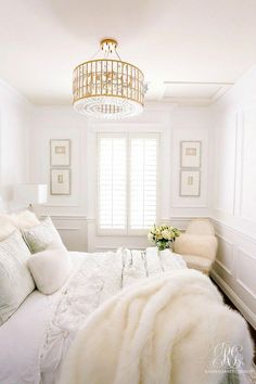 a white bedroom with a chandelier hanging from the ceiling and pillows on the bed