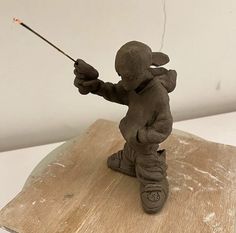 a clay figurine holding a stick on top of a wooden board