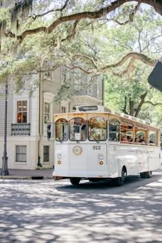 a white bus driving down a street next to a tall building with trees in front of it