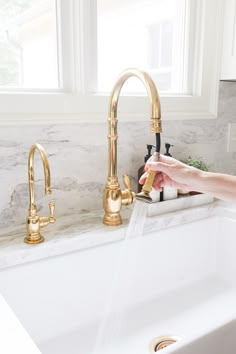 a person washing their hands under a faucet in a kitchen sink with marble counter tops