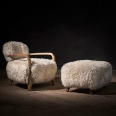 two sheepskin chairs and foot stools on wooden floor in dark room with black background