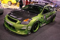 a green car parked in a showroom with other cars behind it and on the ground