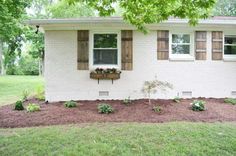 a white brick house with brown shutters and flowers in the window box on the side