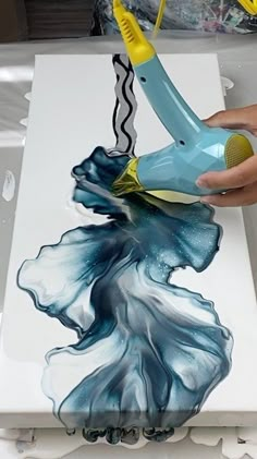 a person using a hair dryer on top of a painting with blue and yellow colors