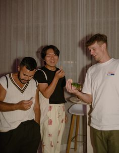 three young men standing next to each other in front of a table with a drink on it