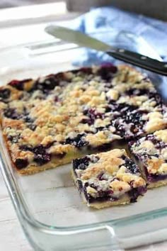 blueberry crumb bars sitting on top of a glass tray next to a knife