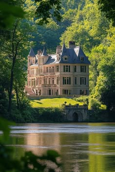 an old house sitting on top of a lush green hillside next to a lake in front of trees