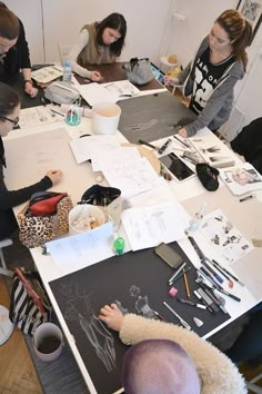 several people sitting at a table working on drawings