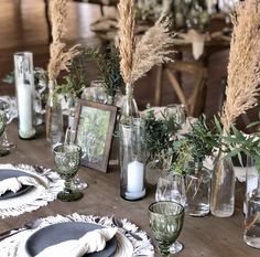 a wooden table topped with lots of plates and vases filled with flowers next to candles