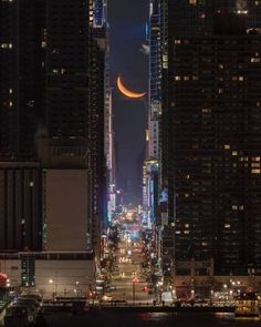 the moon is setting in the sky over a cityscape at night with skyscrapers lit up