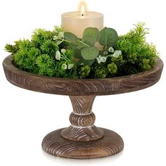 a candle is lit on top of a wooden stand with greenery and foliage in it